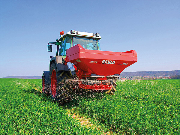 Traktor streut in einem jungen Weizenfeld Dünger.