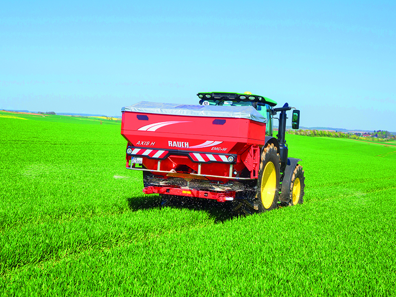 Ein Traktor mit Düngerstreuer fährt über ein Feld